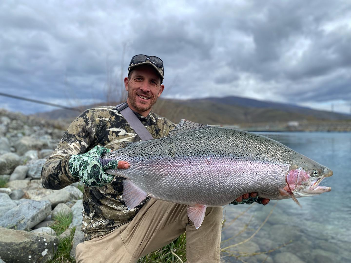 man holding a fish with new zealand mountains in the background